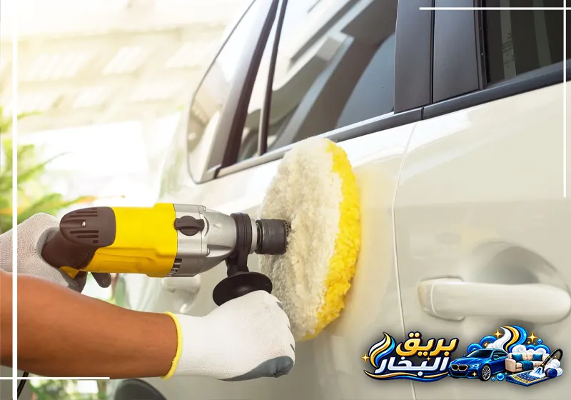 عامل شركة تلميع سيارات بعنك يلمع الباب الخلفي لسيارة بيضاء بآلة كهربائية ووسادة صوفية قرب مقبض الباب