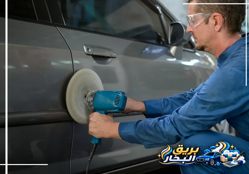 فني شركة تلميع سيارات بعنك يستخدم آلة تلميع بوسادة دائرية بيضاء على باب سيارة رمادية أسفل مقبض الباب
