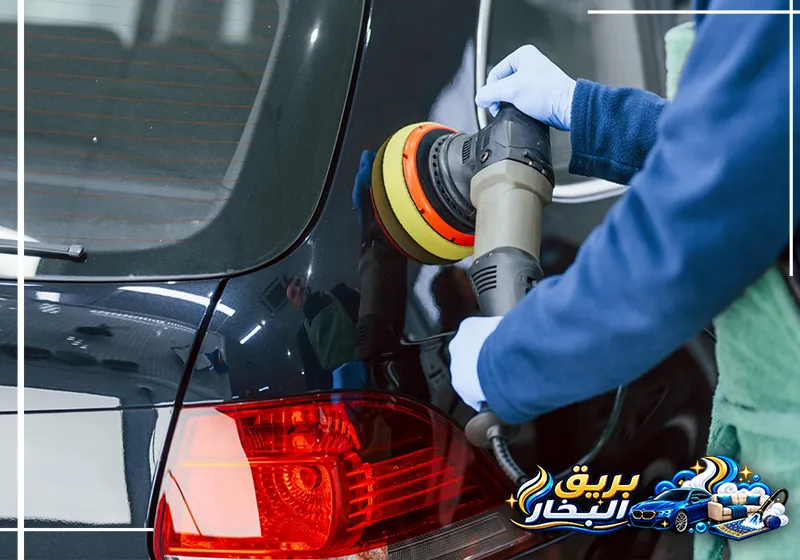 عامل من شركة تلميع سيارات برأس تنورة يستخدم آلة تلميع على جانب سيارة سوداء قرب المصباح الخلفي الأحمر